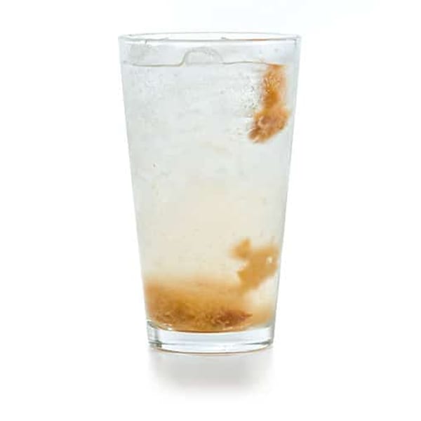 A tall glass of clear Vietnamese soda with brown, syrupy fruit pulp and ice.